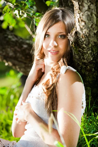 Brunett tjej lutande träd och leende i solstrålarna — Stockfoto