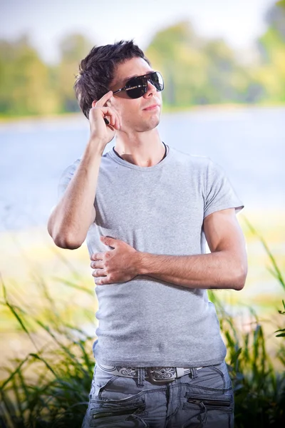 Portrait of handsome man in sunglasses posing against lake — Stock Photo, Image