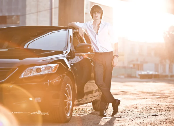 Businessman leaning to luxury black car at sunset rays — Stock Photo, Image