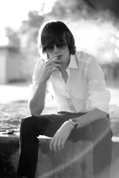 Handsome man in white shirt smoking while sitting on street — Stock Photo, Image