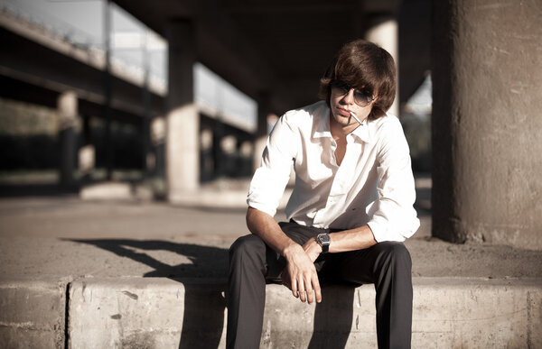 Tired businessman smoking cigarette while sitting on street