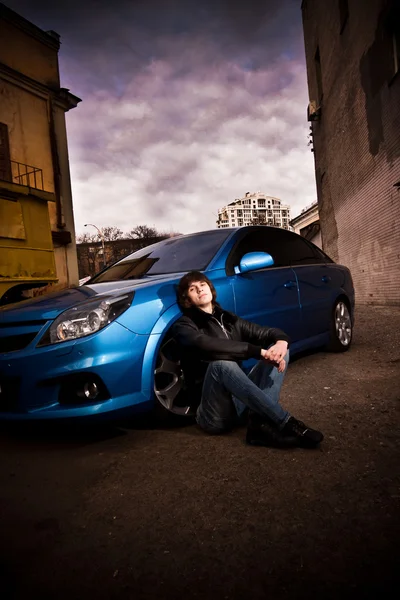 Uomo seduto sulla strada appoggiato al blu sportcar — Foto Stock