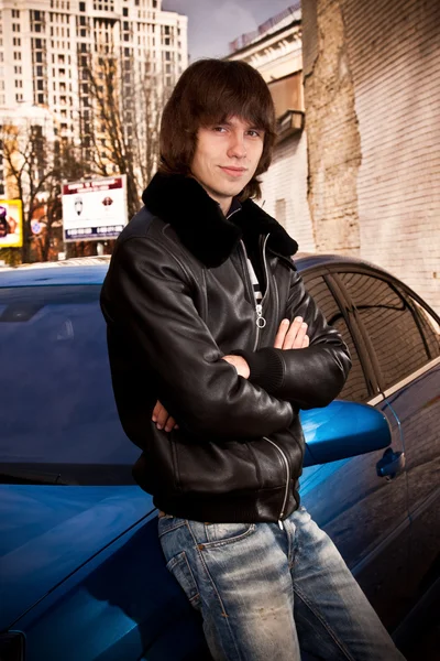 Człowiek w skórzany płaszcz pozowanie w pobliżu niebieski samochód — Zdjęcie stockowe