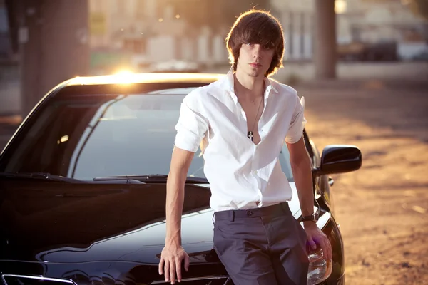 Sexy man in white shirt sitting on car hood on street — Stock Photo, Image