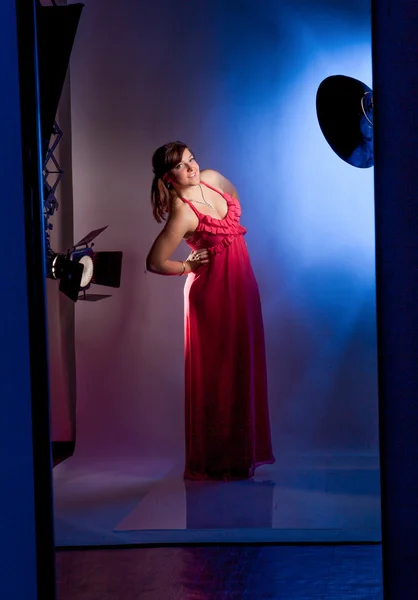 Ung flicka i långa röda klänning poserar i studio mot blixtar — Stockfoto