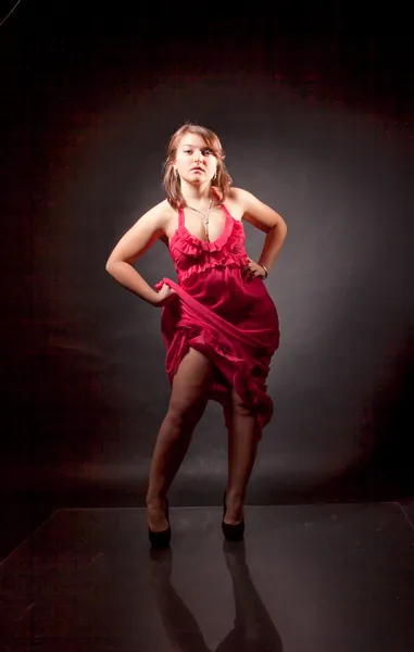 Сексуальная женщина в красном платье, поднимающая юбку и показывающая ногу — стоковое фото