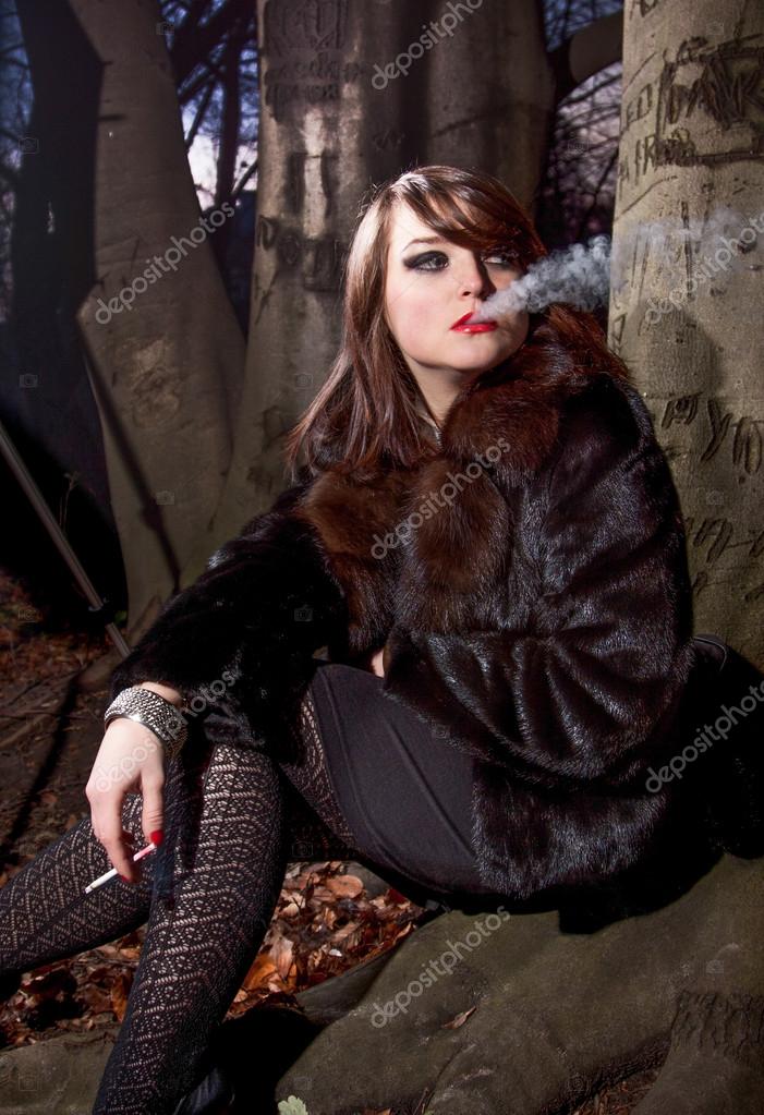 Woman in fur coat smoking cigarette while sitting near big tree Stock ...