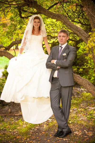 Mariée assise sur une branche d'arbre à côté du marié — Photo