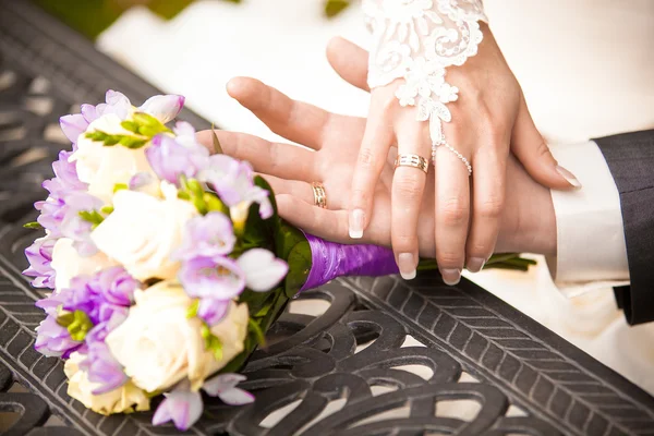 Porträt des Bräutigams, der Bräute Hand in Hand auf dem Tisch neben dem Strauß hält — Stockfoto