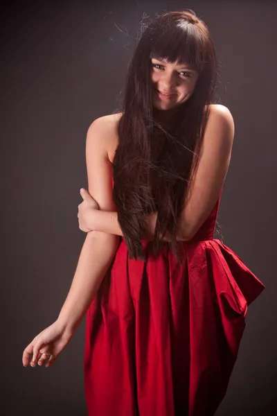 Smiling brunette woman in red dress holding hand on shoulder — Stock Photo, Image