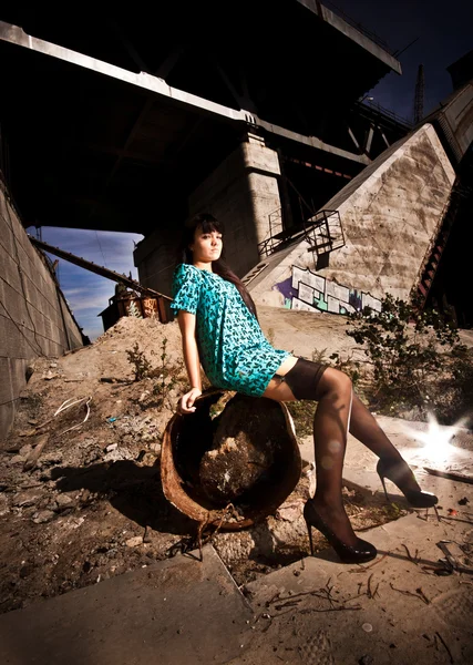 Woman in stockings sitting on rusty barrel at scrapyard — Stock Photo, Image