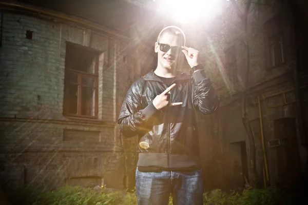 Человек в солнечных очках держит знак победы над старым зданием — стоковое фото
