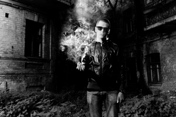 Young man holding cigarette against grungy building — Stock Photo, Image