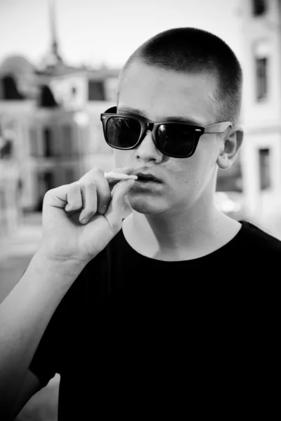 Man in sunglasses smoking cigarette against city landscape — Stock Photo, Image