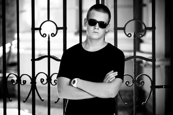 Man in black t-shirt and sunglasses leaning to metal fence — Stock Photo, Image