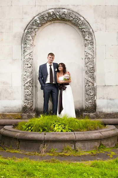 Novia baja y novio alto posando en arco en el parque — Foto de Stock