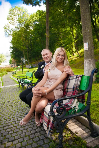 Jong (echt) paar zittend op een bankje in het park en camera kijken — Stockfoto