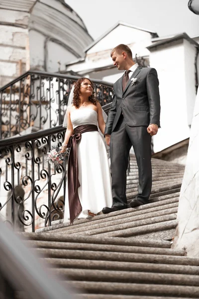 Bride and groom holding hands and walking down the stairs — Stock Photo, Image
