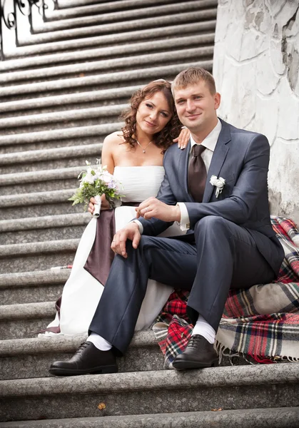 Молодая невеста и жених сидят на лестнице и обнимаются — стоковое фото