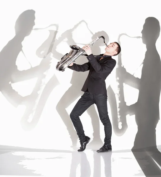 Saxophonist playing against background with shadow of musicians — Stock Photo, Image