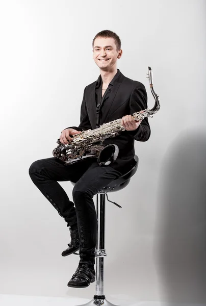 Man i elegant svart kostym med saxofon sitter på stol — Stockfoto