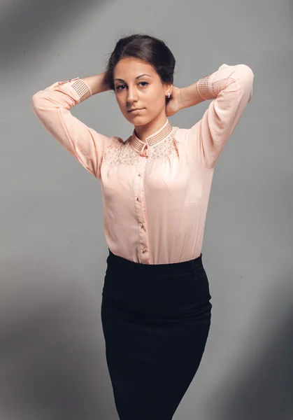 Woman in pink blouse and black skirt posing against grey background — Stock Photo, Image