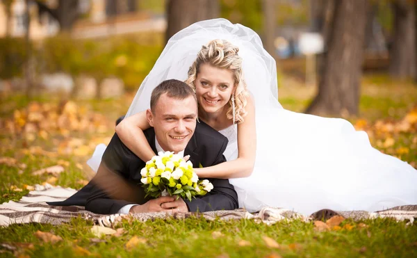 Beautiful bride and groom lying on grass and smiling at camera — Stock Photo, Image