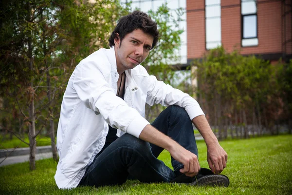 Человек в повседневной одежде сидит на газоне со скрещенными ногами — стоковое фото