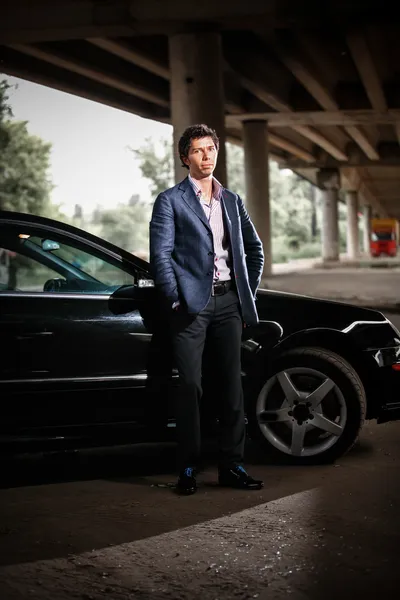 Элегантный мужчина в костюме, позирует против черного роскошного автомобиля — стоковое фото