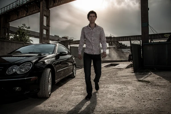 Man walking near black luxury car against industrial background — Stock Photo, Image