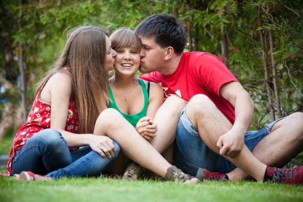 Brother and sister kissing younger sister while sitting on grass — Stock Image Brother and sister kissing younger sister while sitting on grass Stock Image