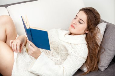 akıllı kadın kanepede yatan ve kitap okuma beyaz kazaklı