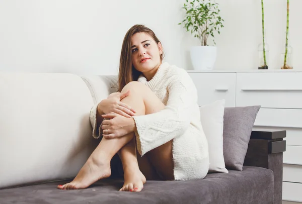 Portrait of brunette woman sitting on sofa in sweater — Stock Photo, Image