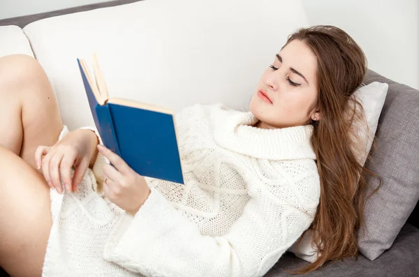 Mujer inteligente en suéter blanco acostado en el sofá y libro de lectura —  Fotos de Stock