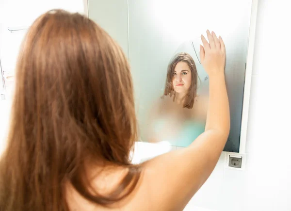 Morena mulher limpeza misted espelho e olhando para a reflexão — Fotografia de Stock