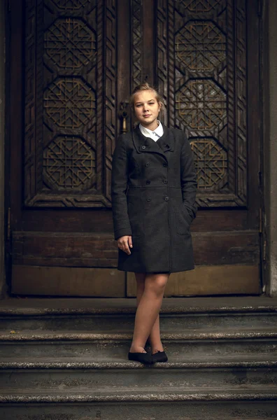 Blondes Mädchen steht alte Treppe in schwarzem Regenmantel — Stockfoto