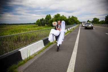 Young groom carrying on hands slim bride on road clipart