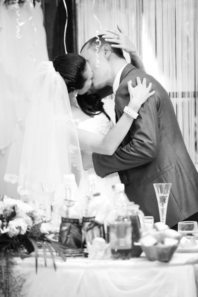 Casal recém-casado beijando no restaurante atrás da mesa — Fotografia de Stock