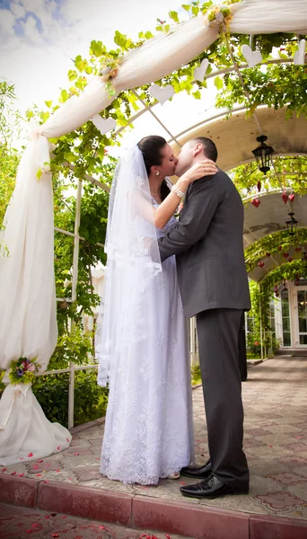 Bruid en bruidegom knuffelen en zoenen onder huwelijksboog — Stockfoto