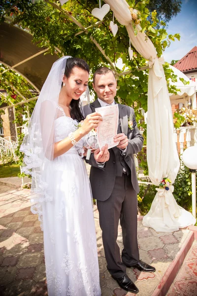 Sposa che tiene contratto di matrimonio sotto arco a parco — Foto Stock