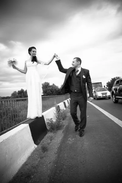 Photo of man holding brides hand balancing on edge of road — Stock Photo, Image