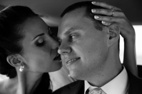 Black and white portrait of brunette bride kissing groom in cheek — Stock Photo, Image