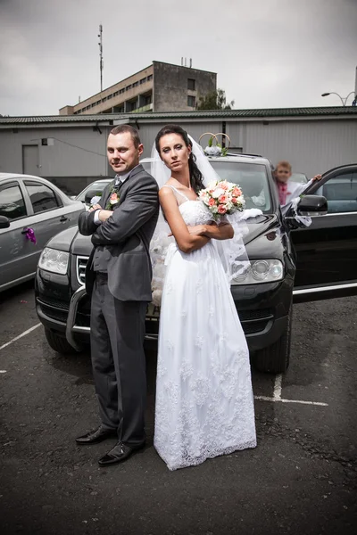 Bride and groom standing back to back on car parking — Stock Photo, Image