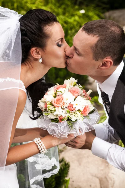 Casal beijando apaixonadamente e segurando buquê de casamento — Fotografia de Stock