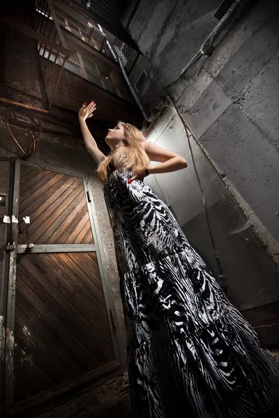 Blonde woman in dress lifting hand up against big building — Stock Photo, Image