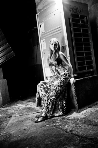 Sexy woman sitting on abandoned street with metal constructions — Stock Photo, Image