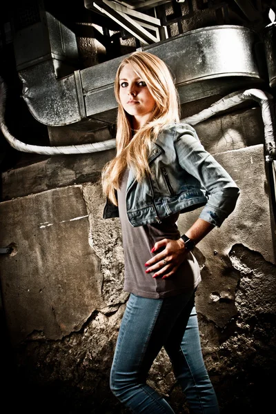 Woman in jeans and coat walking against grungy industrial building — Stock Photo, Image