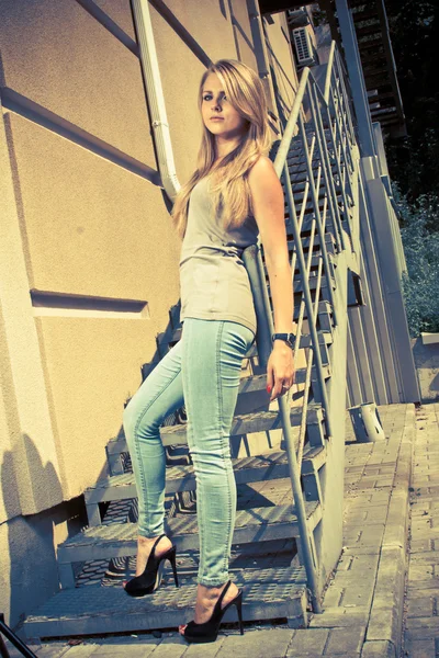 Sexy woman in jeans and heels leaning against metal railings — Stock Photo, Image