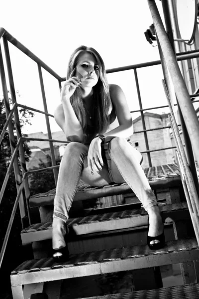 Sexy woman in jeans sitting on top step of metal staircase — Stock Photo, Image