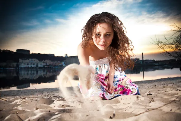 Kumsalda oturuyor ve kum atma içinde kıvırcık kadın — Stok fotoğraf